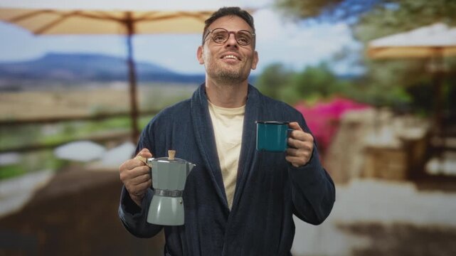 Man in robe holds a moka pot and raises a teal coffee mug to his nose on a building terrace, eyes closed; morning serenity.