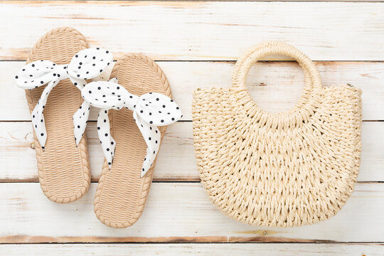 Straw bag with sandals on wooden background, top view