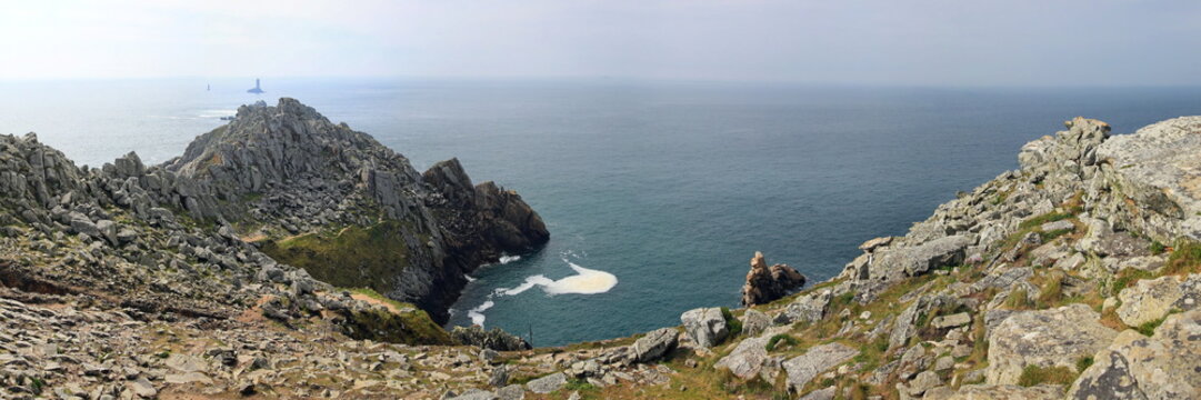 Raue Felsklippen fallen steil in den Atlantik ab, w&auml;hrend im Hintergrund die ber&uuml;hmten Leuchtt&uuml;rme Phare de la Vieille und T&eacute;vennec aus den unruhigen Wellen ragen.
