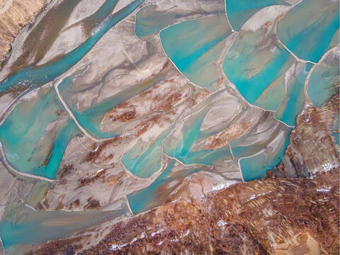 Aerial view of turquoise glacial meltwater pools and braided river channels flowing through the arid mountain landscape of Booni in Chitral, Khyber Pakhtunkhwa, Pakistan.