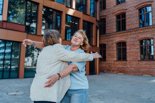 Joyful Senior Woman Opening Arms Toward Middle Aged Friend Outdoors