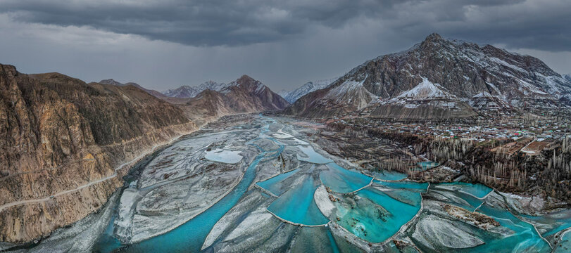 Aerial view of turquoise river channels flowing through a mountain valley with snow-dusted peaks and a small village Chitral, Khyber Pakhtunkhwa, Pakistan.