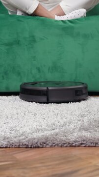 Slow motion of modern robotic vacuum cleaner which moving on fluffy carpet and cleaning it from dust and facilitating to keep clean in house