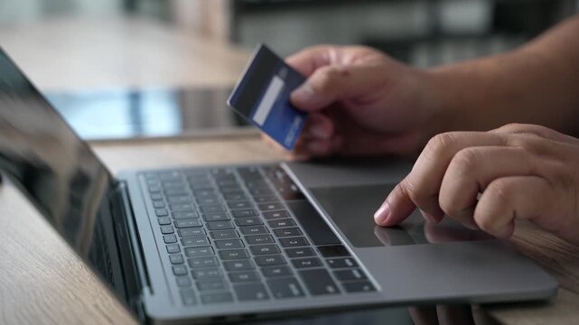 Hand holding a credit card while using a laptop to complete an online purchase and digital payment transaction, illustrating ecommerce checkout, internet shopping, banking, and cashless consumer spend