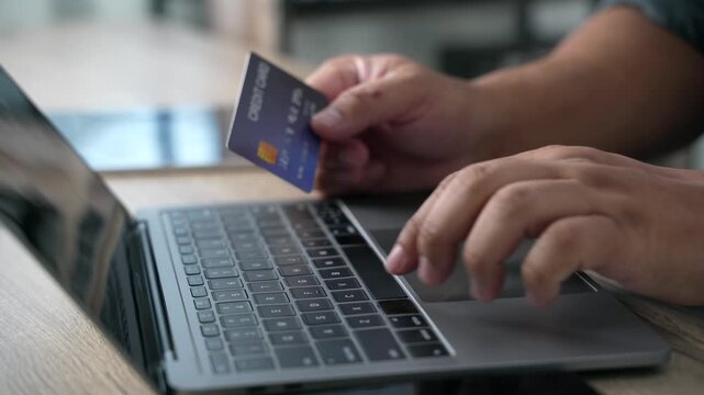 Hand holding a credit card while using a laptop to complete an online purchase and digital payment transaction, illustrating ecommerce checkout, internet shopping, banking, and cashless consumer spend