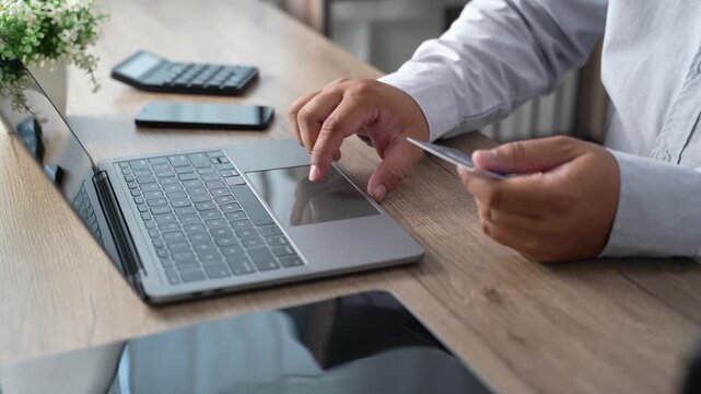 Hand holding a credit card while using a laptop to complete an online purchase and digital payment transaction, illustrating ecommerce checkout, internet shopping, banking, and cashless consumer spend