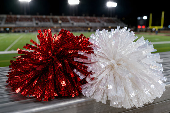 Red and white cheerleading pompoms lying on stadium bench at night, close-up with football field background