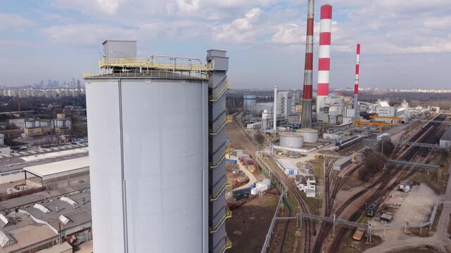 Close Aerial Warszawa Storage Tank Engineering Shot With Cylindrical Structure, Access Ladder And Platform, Surrounding Rail Yard And Distant Chimneys, Industrial Inspection And Maintenance