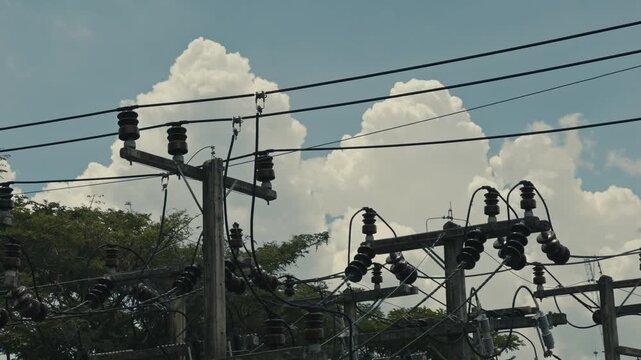 Detailed close up of an electricity pole top featuring primary distribution wires, insulators and utility components against a clear blue sky in an energy infrastructure setting.