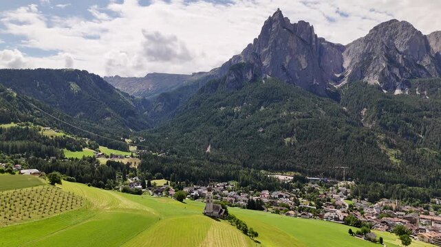 Sweeping 4K drone footage over the charming historic town of Castelrotto, showcasing the iconic St. Valentin Church bell tower framed by the majestic peaks of the Dolomites, South Tyrol.