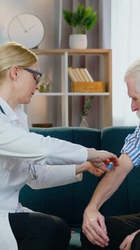 Healthcare concept where good-natured smiling friendly qualified woman-doctor doing injection of vaccine to mature bearded male patient when visiting him on home treatment