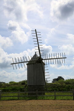 Historische Windm&uuml;hle Moulin de Trouguer aus Naturstein in der Bretagne unter blauem Himmel mit imposanten Holzfl&uuml;geln und einem liegenden M&uuml;hlstein im gr&uuml;nen Gras.
