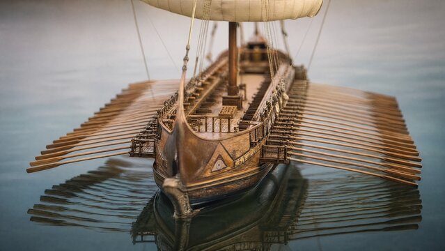 trireme. Miniature ancient trireme galley with parallel oars on a calm sea. mobility guides, transit brochures, designed for mobility and urban transit guides, improves user orientation.