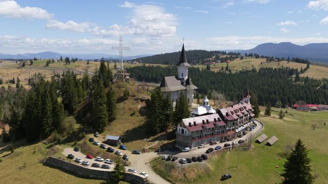 Aerial drone view of the monastery complex in Dorna Arini, featuring traditional wooden architecture, tall church towers, and surrounding mountain landscape