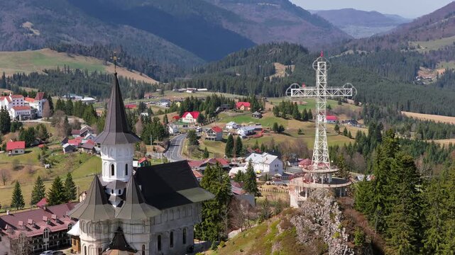 Aerial drone view of the large metal cross and Romanian flag near Acoperamantul Maicii Domnului Monastery in Dorna Arini