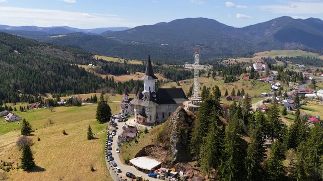 Aerial drone view of the large metal cross and Romanian flag near Acoperamantul Maicii Domnului Monastery in Dorna Arini