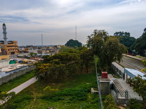 Aerial view of the Golra Railway Station area featuring train tracks, lush green trees, and urban buildings under a cloudy sky in Islamabad, Islamabad Capital Ter, Pakistan.