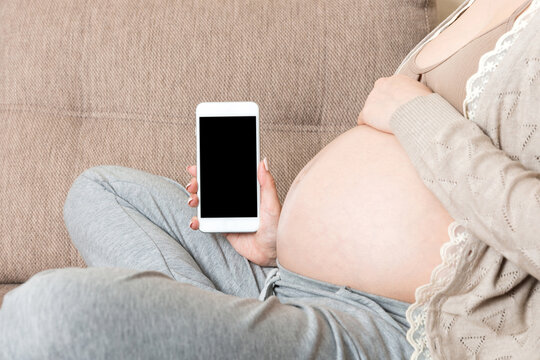 Pregnant woman showing smartphone with black screen in sofa