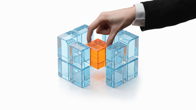 Hand placing orange cube between volumetric blue glass structures. Concept of bridge building, cybersecurity, fintech integration, banking systems, consulting and SaaS platforms.