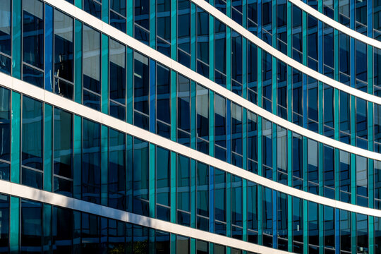 Curved white lines cross a blue glass office facade, where windows, reflection and grid rhythm shape the urban building surface along the city edge