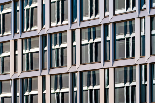 Repeating office windows fill a facade grid, where glass, reflection and white frames turn urban architecture into a clean business pattern