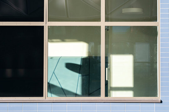A single window breaks a pale facade grid, where glass reflection, shadow and interior detail create quiet urban architecture geometry