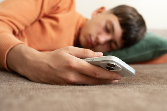 Sleeping teenager holding smartphone in hand on sofa. Concept of excessive screen time, digital fatigue, technology overuse, unhealthy habits, rest and modern lifestyle.