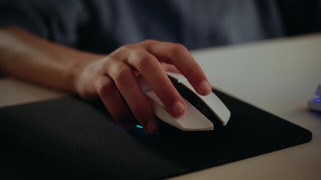 Close-up of a person's hand using a white computer mouse with RGB lighting while playing a video game or working on a computer.