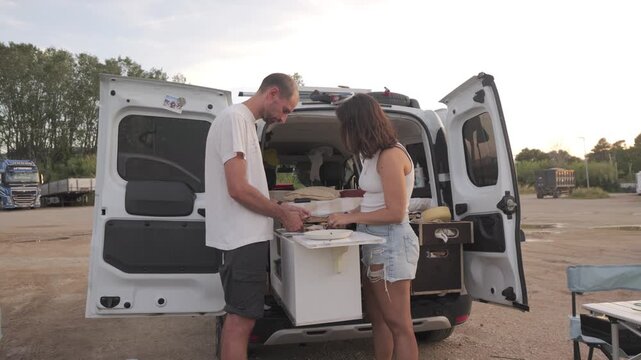 Wide shot couple cooking in van life outdoor setup, Italy