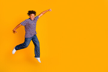 Naklejka premium Joyful boy jumping in striped t-shirt and jeans on bright orange background, energetic playful childhood moment with an expressive smile