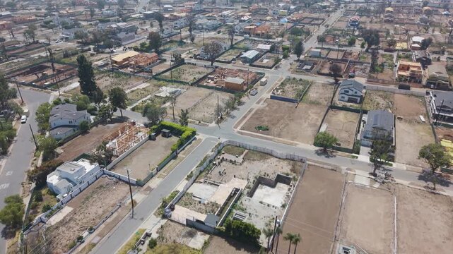 Wildfire devastation with empty lots and burned foundations filling residential blocks, scattered surviving homes and bare trees along streets under hazy sky. California, USA. Aerial view.