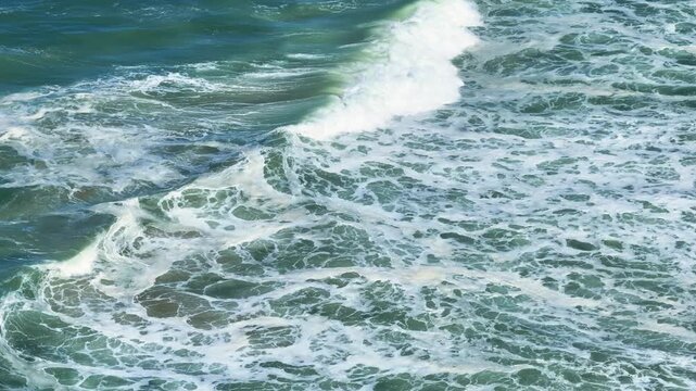 Waves crash on the sandy beach along the Atlantic coast. Aerial view shows the coastline and shoreline. Ocean water reflects sunlight. Coastal dunes outline the beach area.