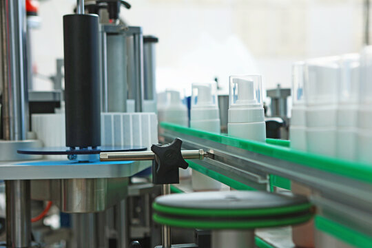 White plastic bottles without labels on conveyor belt. Conveyor belt for cosmetics production. Labeling machine. Cosmetics production