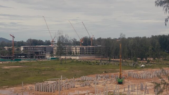 Active construction site featuring concrete foundation poles, tower cranes and apartment complexes under development, showcasing urban growth and residential expansion.