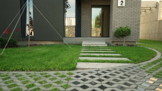 Permeable paving system with turfstone pavers and grass growing through the grids creating a durable and eco-friendly driveway leading to a modern gray brick house exterior