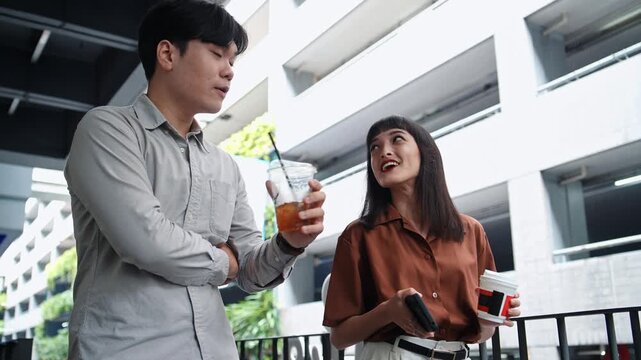 Asian man and woman employee colleague holding coffee cup talking during lunch break in the city