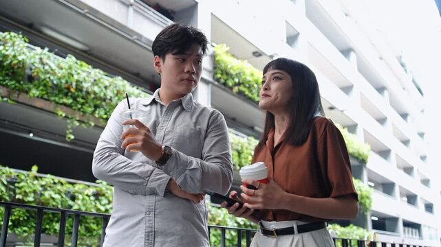 Asian employee colleague holding coffee cup talking during lunch break in the city