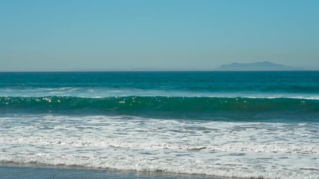 Blue ocean waves roll on Channelside beach with an island on the horizon