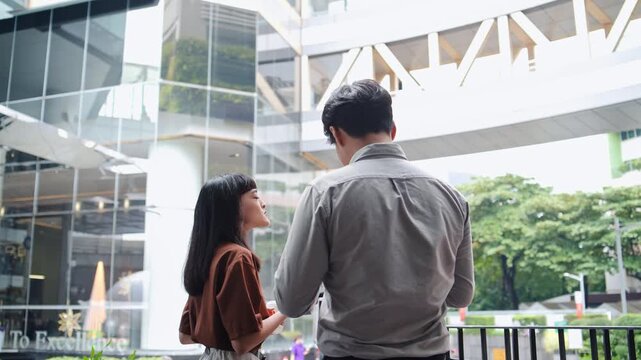 Rear view of young Asian business professional looking up at office building corporate campus walkway, woman standing next to man while planning commercial real estate development project
