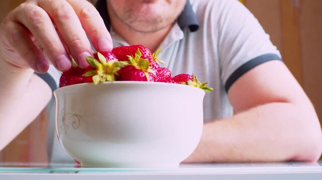 Low angle close-up.Man eating fresh strawberries from a bowl. Blurred man silhouette. Shallow DoF, natural window light. Healthy nutrition, organic food, vitamins and clean lifestyle.