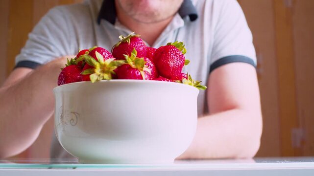 Cinematic closeup.Man enjoying ripe berries at home. Defocused middle-aged man silhouette. Soft focus, morning daylight.Healthy nutrition - organic food. 