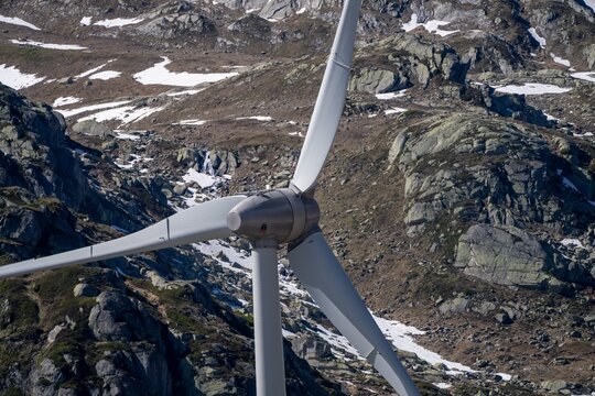 Aerial view of the Gotthard Wind Farm turbine blades and hub against the rugged rocky slopes and snow patches of the Swiss Alps in Airolo, Ticino, Switzerland.