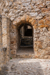 Fototapeta premium An ancient stone wall with a medieval arched tunnel entrance and stairs inside a historic castle fortress