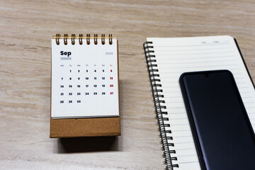 Top view of September 2026 desk calendar with smartphone and blank spiral notebook on wooden table. Copy space for time management, event planning, or schedule concept. © IgnasiusIMade