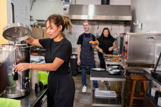 Female barista preparing coffee in busy restaurant kitchen