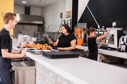 Baristas preparing espresso drinks and churros at cafe counter