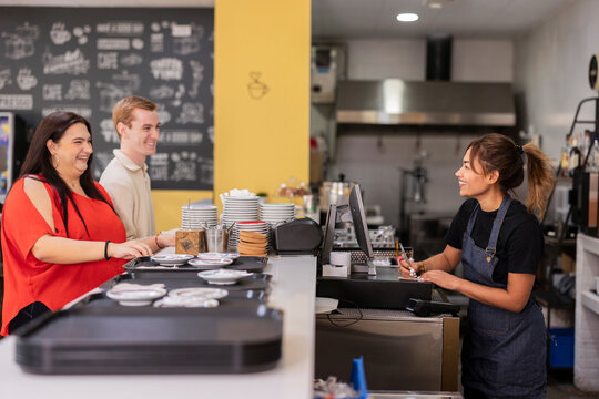 Smiling customers ordering coffee at a modern cafe counter