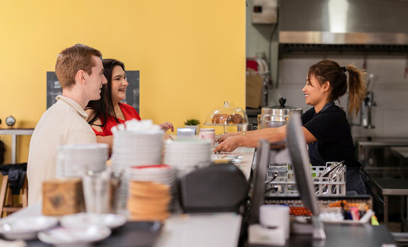 Barista serving coffee to customers at modern cafe counter