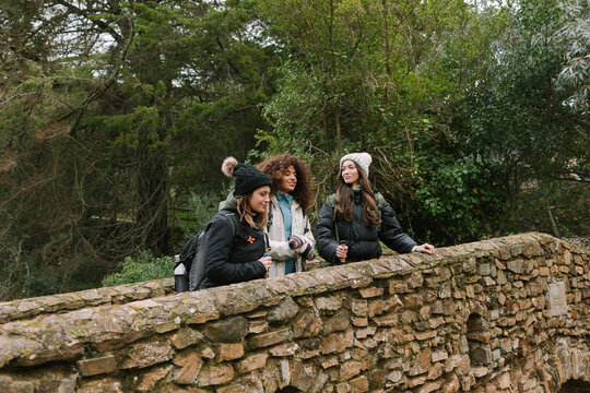 Winter hiking friends pause on stone bridge in mountain forest