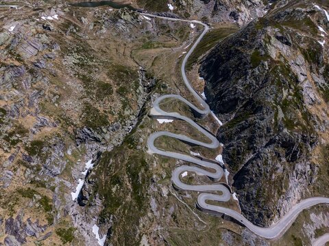 Aerial view of the winding Tremola road with its iconic hairpin turns snaking through the rocky alpine landscape and patches of snow in Airolo, Ticino, Switzerland.